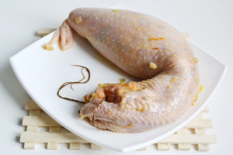 Securing the Homemade Sausage with Kitchen Twine A raw homemade chicken sausage being tied securely at both ends with kitchen twine.