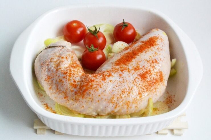 Placing the Sausage in a Baking Dish with Onions and Tomatoes The raw chicken sausage placed on a bed of onion rings in a baking dish, ready for the oven.