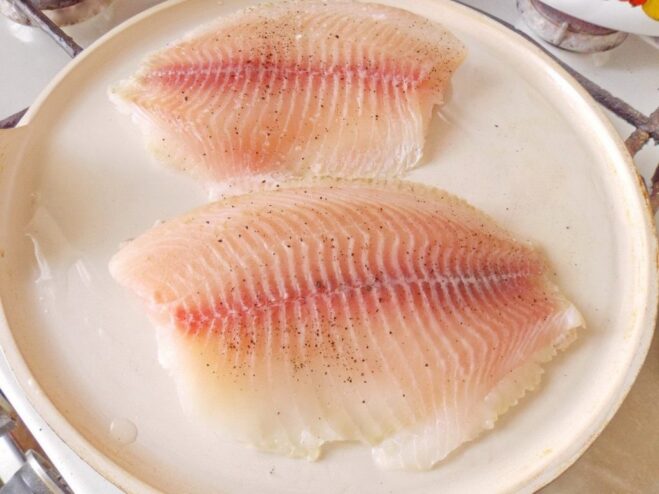 Properly prepping the fish fillet is key to a crispy skin Raw ocean perch fillets on a cutting board, being patted dry and seasoned with salt and pepper.