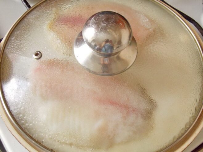 Covering the pan helps the fish cook evenly Fish fillet frying in a pan, covered with a glass lid to cook through.