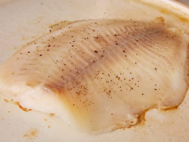 A light coat of oil prevents the fish from sticking A hand brushing a raw ocean perch fillet with vegetable oil before frying.