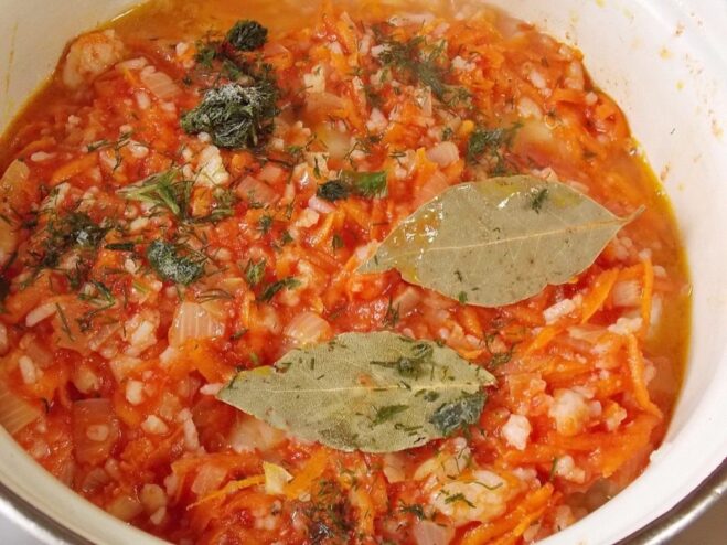 Simmering Golubtsy in a Rich Tomato Sauce Cabbage rolls in a pot being covered with a tomato and vegetable sauce before simmering.