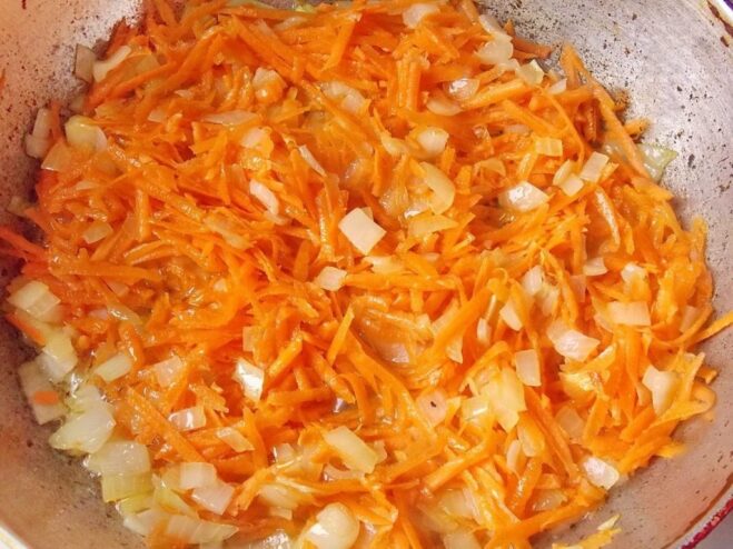 Building Flavor for the Filling: Adding Carrots Grated carrots being added to the sautéed onions in a pan to create the vegetable base.