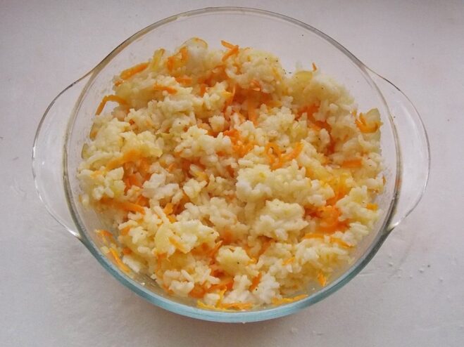 Preparing the Vegetable and Rice Filling for Golubtsy A bowl of cooked rice mixed with sautéed onions and carrots, creating the filling for the cabbage rolls.