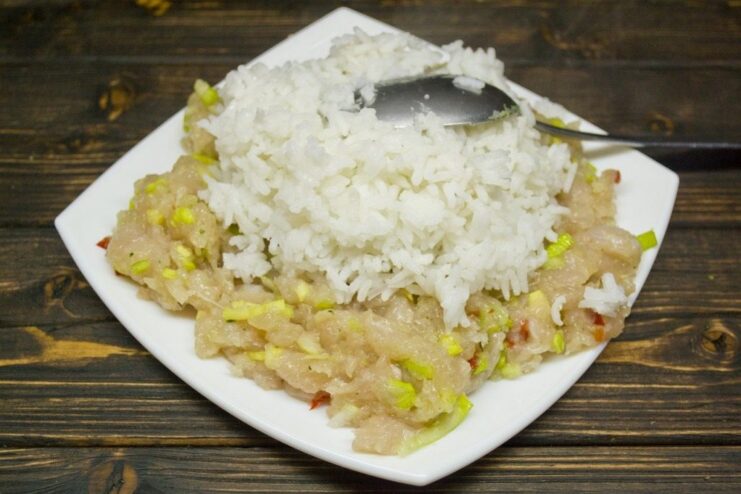 A bowl with minced chicken, cooked rice, and spices being mixed for the golubtsy filling.