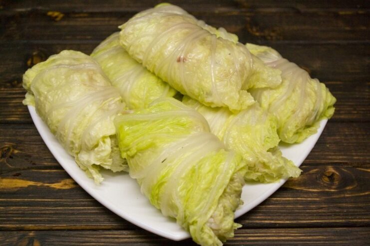 A hand wrapping a filling of minced meat and rice into a blanched Napa cabbage leaf.