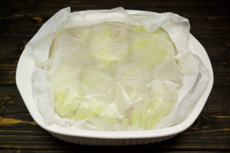Uncooked golubtsy arranged tightly in a baking dish, covered with parchment paper.