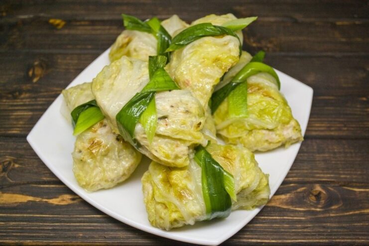 A close-up of a cooked cabbage roll being tied with a green leek strip for decoration.