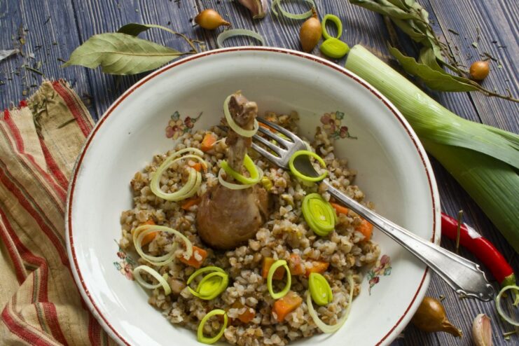 A serving of oven-baked grechka with chicken in a clay pot, garnished with herbs.