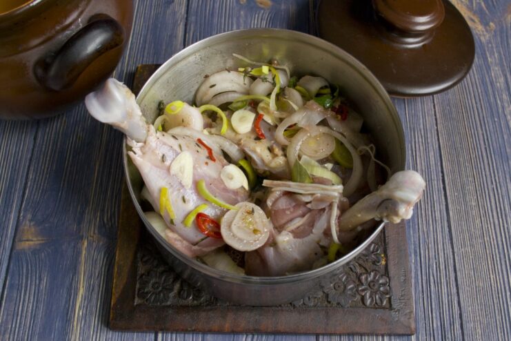 Raw chicken pieces in a glass bowl with marinade ingredients like onions and herbs.