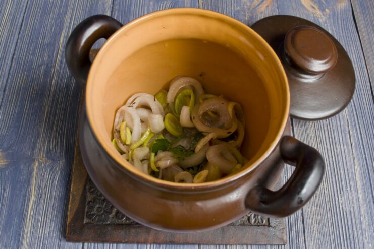 A clay pot with a layer of butter and marinated onions at the bottom.