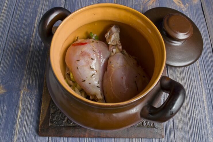Marinated chicken pieces being layered over onions in a clay pot.