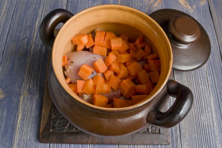 Fresh carrots being chopped into large cubes on a cutting board.