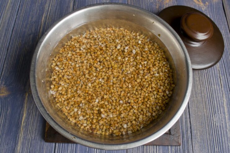 Buckwheat groats being rinsed in a sieve under running water.