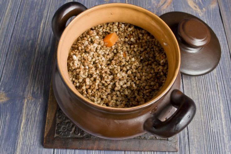 Rinsed buckwheat being added to the clay pot on top of the chicken.