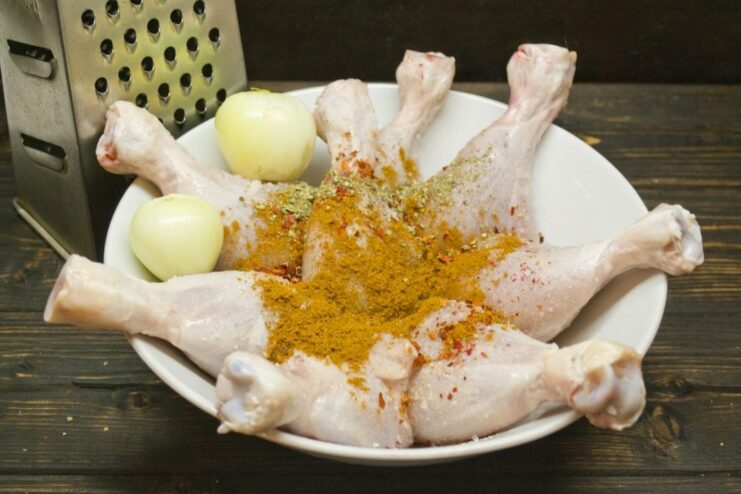 Flavor Infusion: Marinating Chicken Legs in Aromatic Spices Raw chicken legs in a bowl, coated with a spice marinade of onions and herbs.