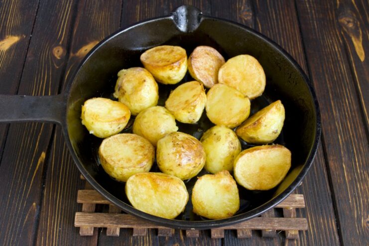 Slices of boiled new potatoes being fried until golden brown. Close-up of boiled potato slices being fried to a golden crust in a pan.
