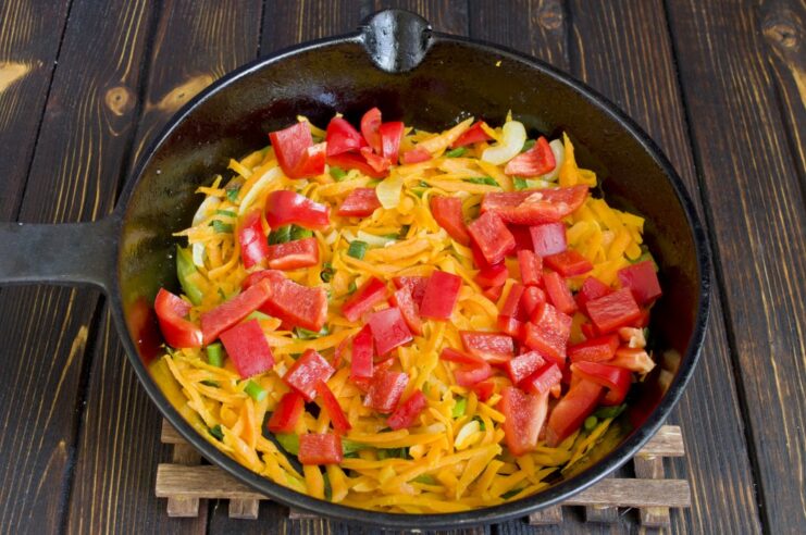 Cooking diced bell peppers with carrots and onions. Diced red bell pepper added to the pan with carrots and onions to simmer.