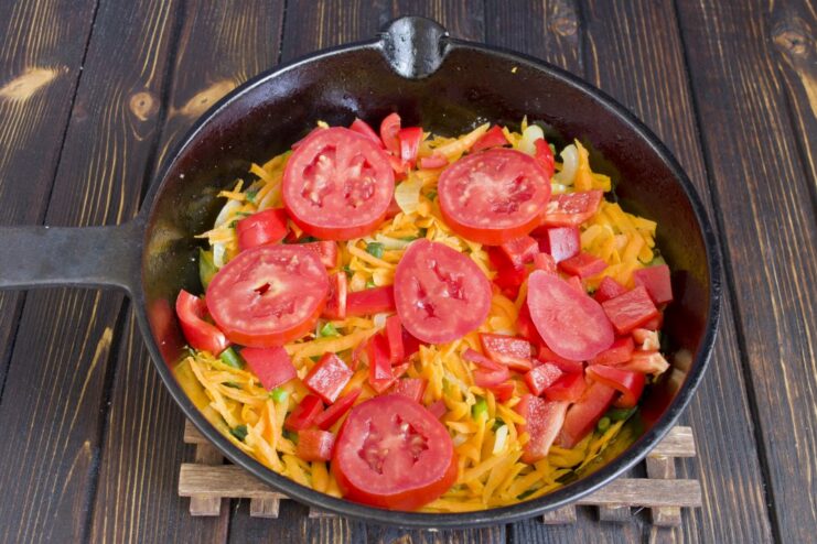 Simmering sliced tomatoes with the rest of the vegetables. Thinly sliced tomatoes layered over the vegetable mix in the pan, simmering.
