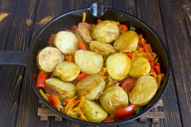 Returning the golden-fried potatoes to the pan with the vegetables. Fried potato slices being added back into the pan on top of the cooked vegetables.