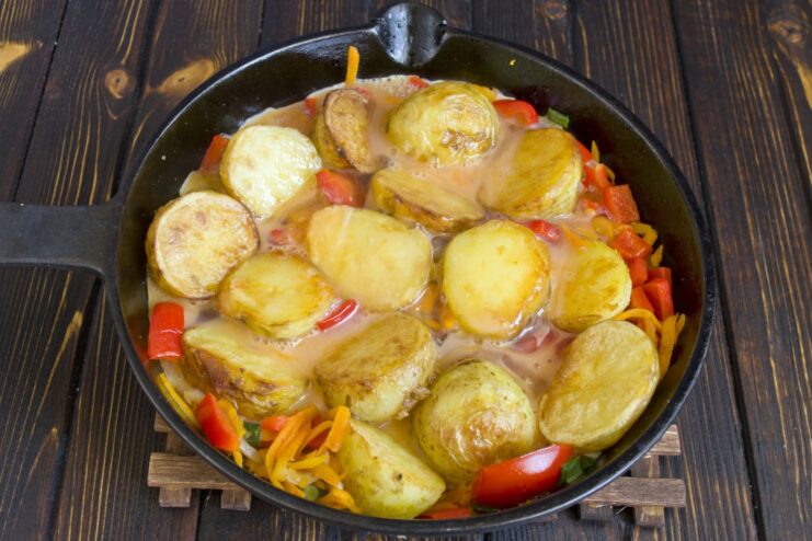 Pouring the whisked egg mixture over the potatoes and vegetables. Whisked eggs being poured over the potato and vegetable mixture in the pan.