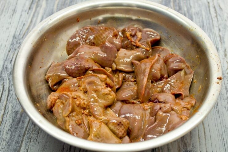 Marinating Chicken Liver in Spices Raw chicken liver pieces in a bowl with salt and red pepper seasoning.