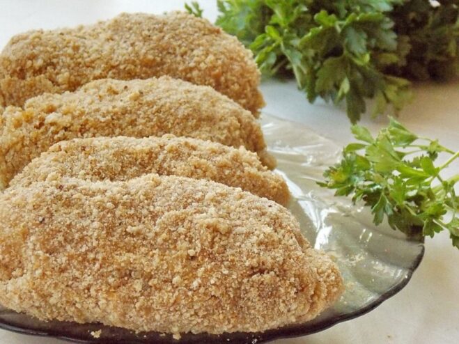 Chilling the Cutlets Before Frying is Key Several breaded Chicken Kyiv cutlets on a plate being placed in the freezer to firm up.
