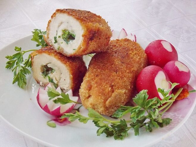 A plate of golden-brown, crispy Chicken Kyiv, garnished with fresh herbs and ready to be served.