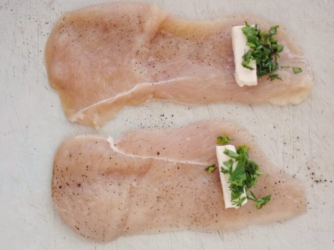 Filling the Chicken Fillet with Herb Butter A flattened chicken fillet with a stick of frozen butter and chopped herbs placed on top.