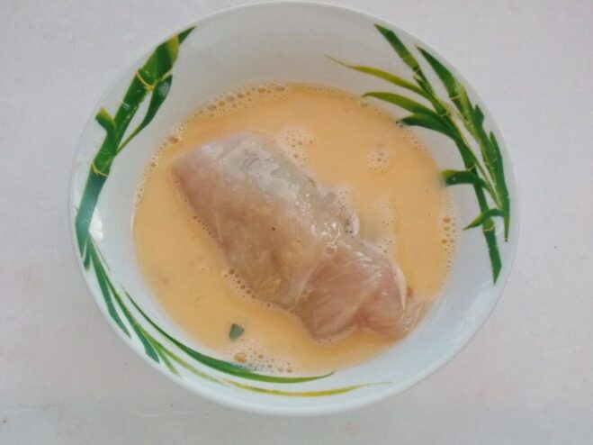 First Step of Breading: The Egg Wash A rolled chicken cutlet being dipped into a bowl of whisked eggs.