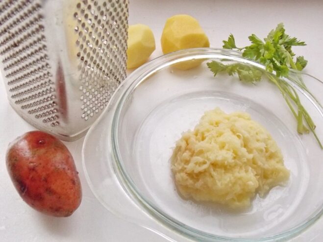 A hand grating a raw potato on a fine metal grater.