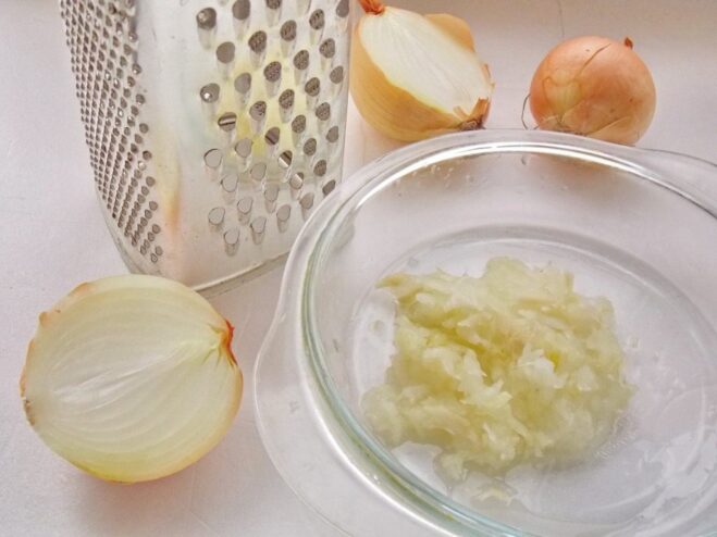A hand grating an onion on a coarse metal grater.