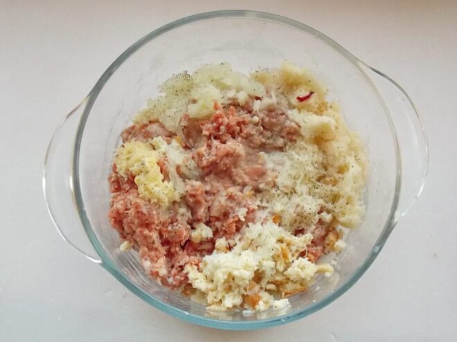 A bowl of ground meat mixture with grated vegetables being mixed by hand.