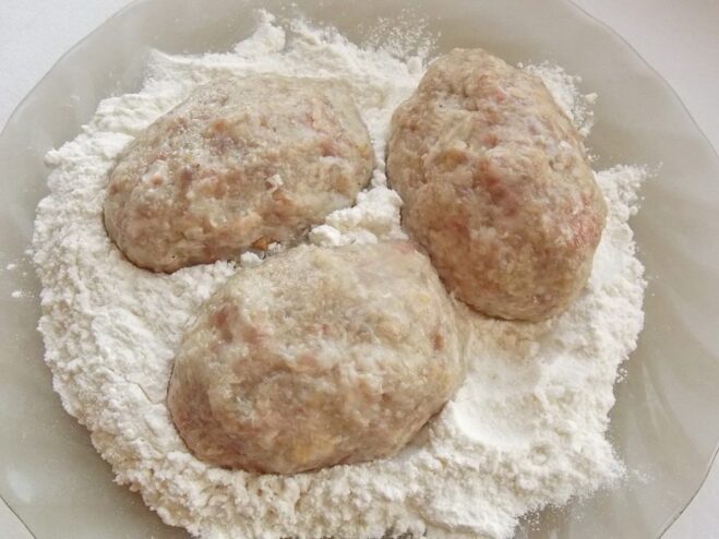 Raw formed kotlety being dredged in a plate of white flour before frying.