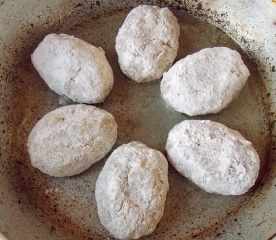 Raw kotlety being placed into a hot frying pan with sizzling oil.