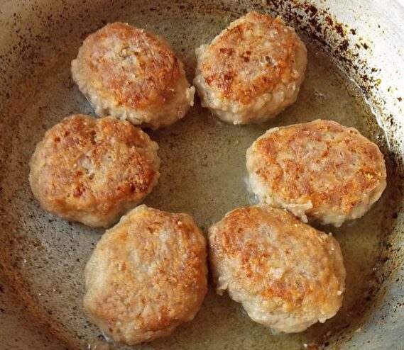 Golden-brown kotlety being flipped with a fork in a frying pan.
