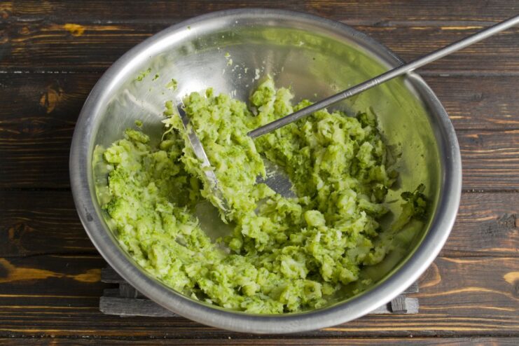 Mashing Steamed Broccoli for the Patties Steamed broccoli being mashed into a coarse puree in a bowl.