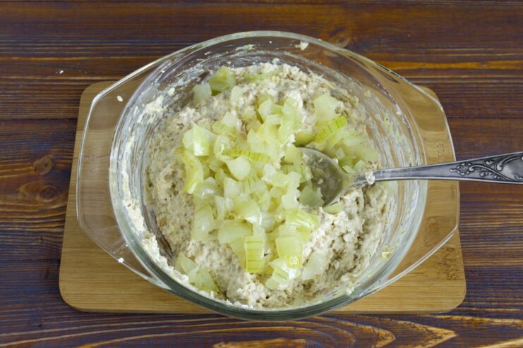 Sautéed onions being added to the bowl of soaked rolled oats.