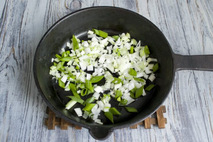 Finely chopped green onions being sautéed in a hot skillet.