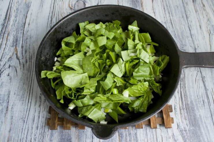 Fresh spinach wilting in a skillet with sautéed green onions.