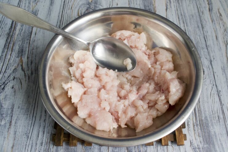 Fresh chicken fillet being processed through a meat grinder.