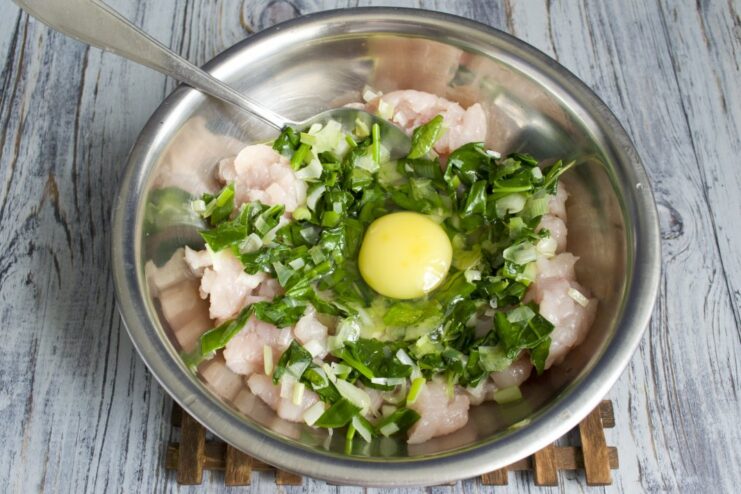 A raw egg cracked into the bowl with the chicken and spinach mixture.