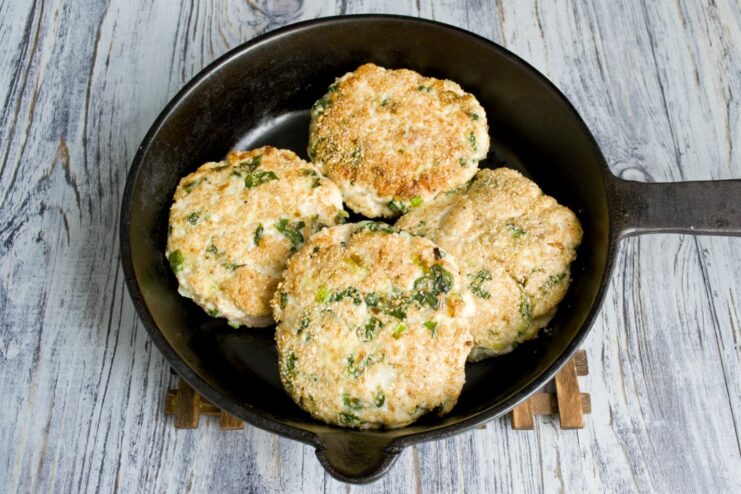 Four chicken and spinach cutlets sizzling in a skillet, turning golden brown.