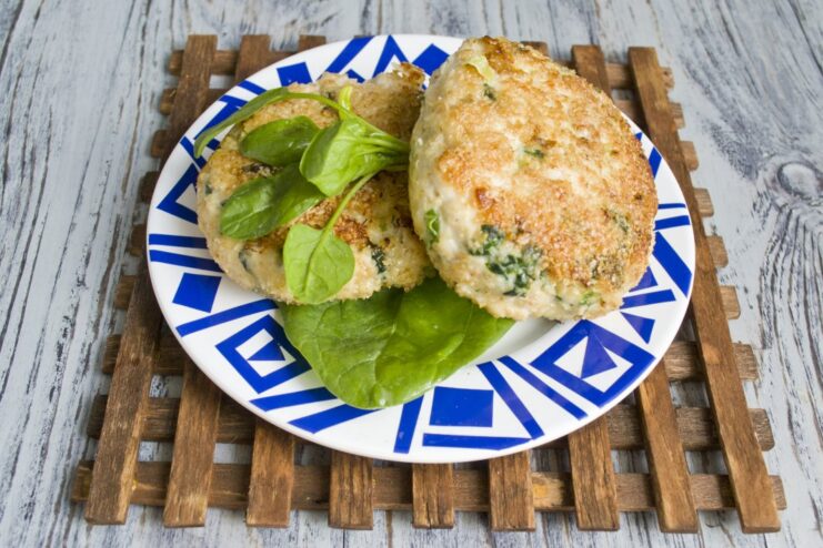 A close-up of a cooked chicken and spinach cutlet on a plate, showing its juicy texture.