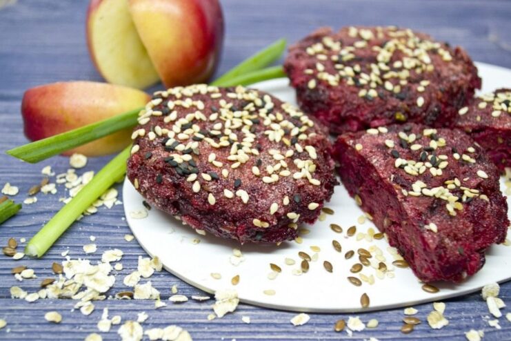 A plate of finished beetroot patties with apples and flax seeds, garnished with sesame seeds and green onions.