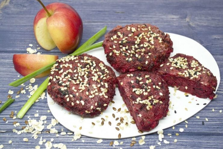 A plate of finished beetroot patties with apples and flax seeds, garnished with sesame seeds and green onions.