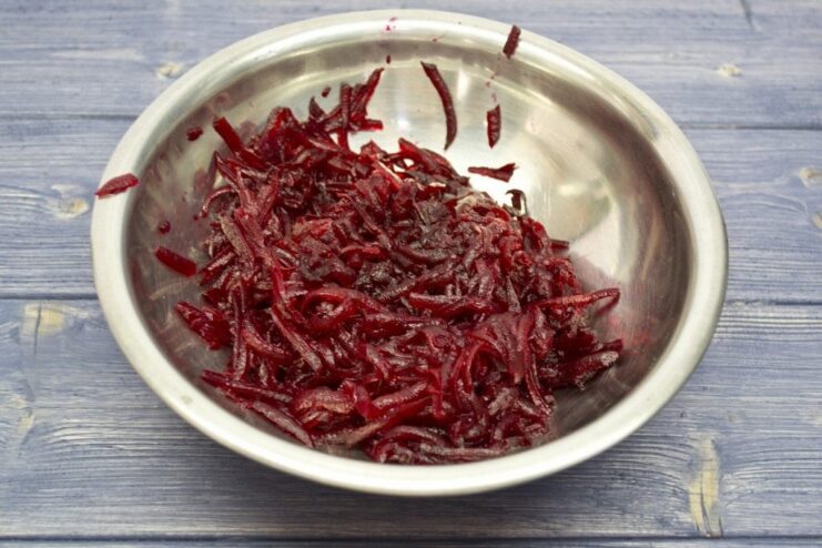 Close-up of boiled beetroot being grated on a coarse grater into a bowl.