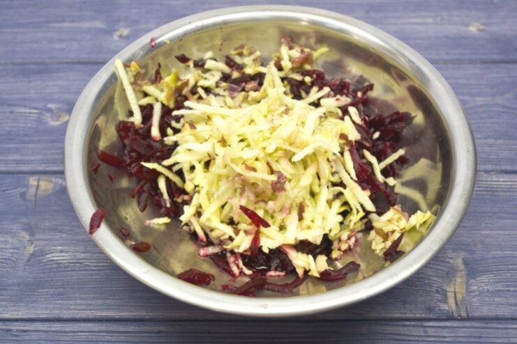 Grated apples being added to a bowl of grated beetroot.