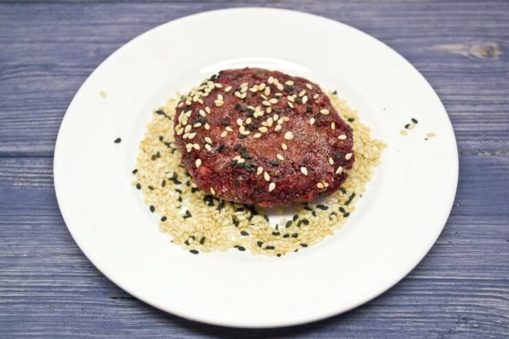 Finished beetroot patties being rolled in a mixture of white and black toasted sesame seeds.
