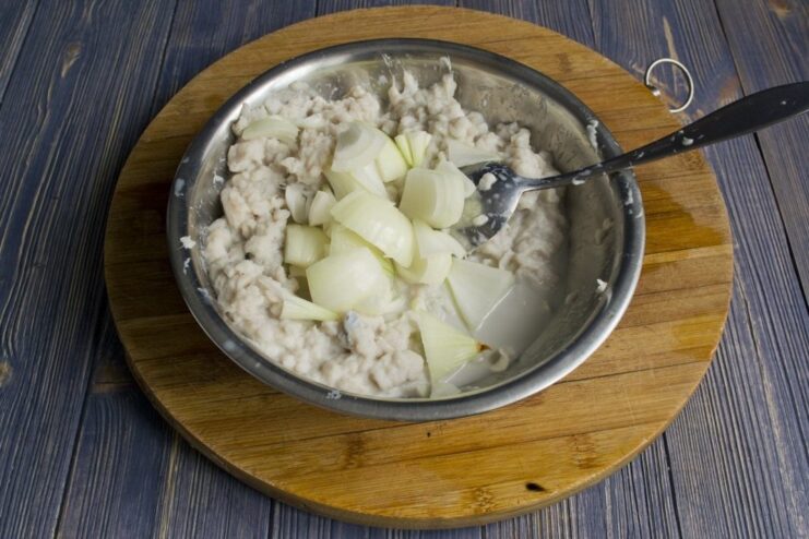 Adding onion to the fish mixture Diced onion being added to the ground cod mixture in a bowl.